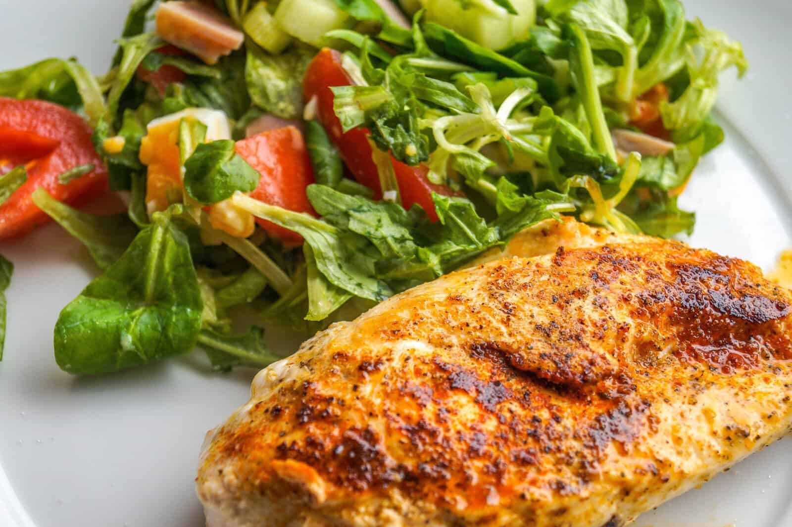 chicken breast next to a green salad on a white plate