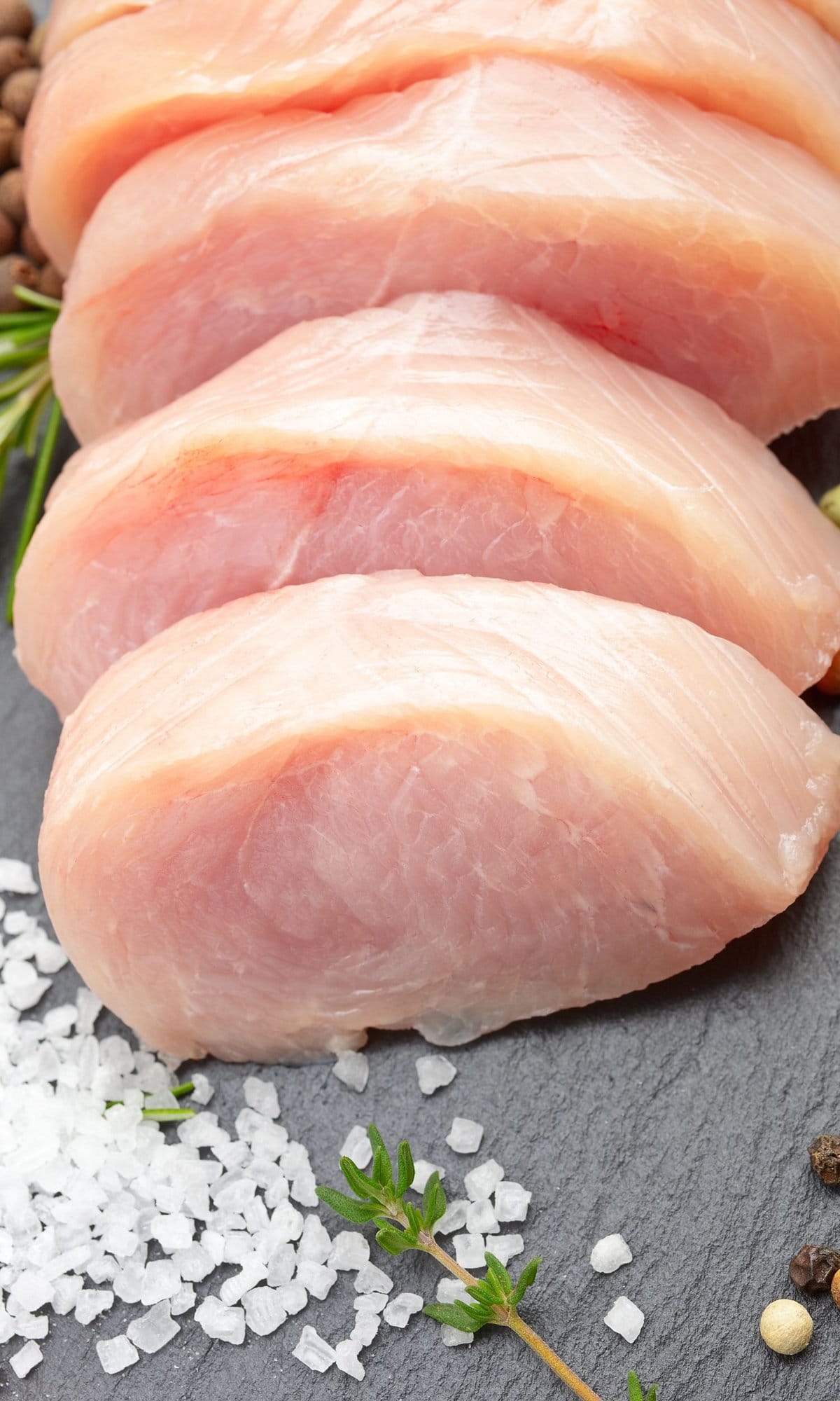 raw sliced chicken on a gray surface next to crystalized salt