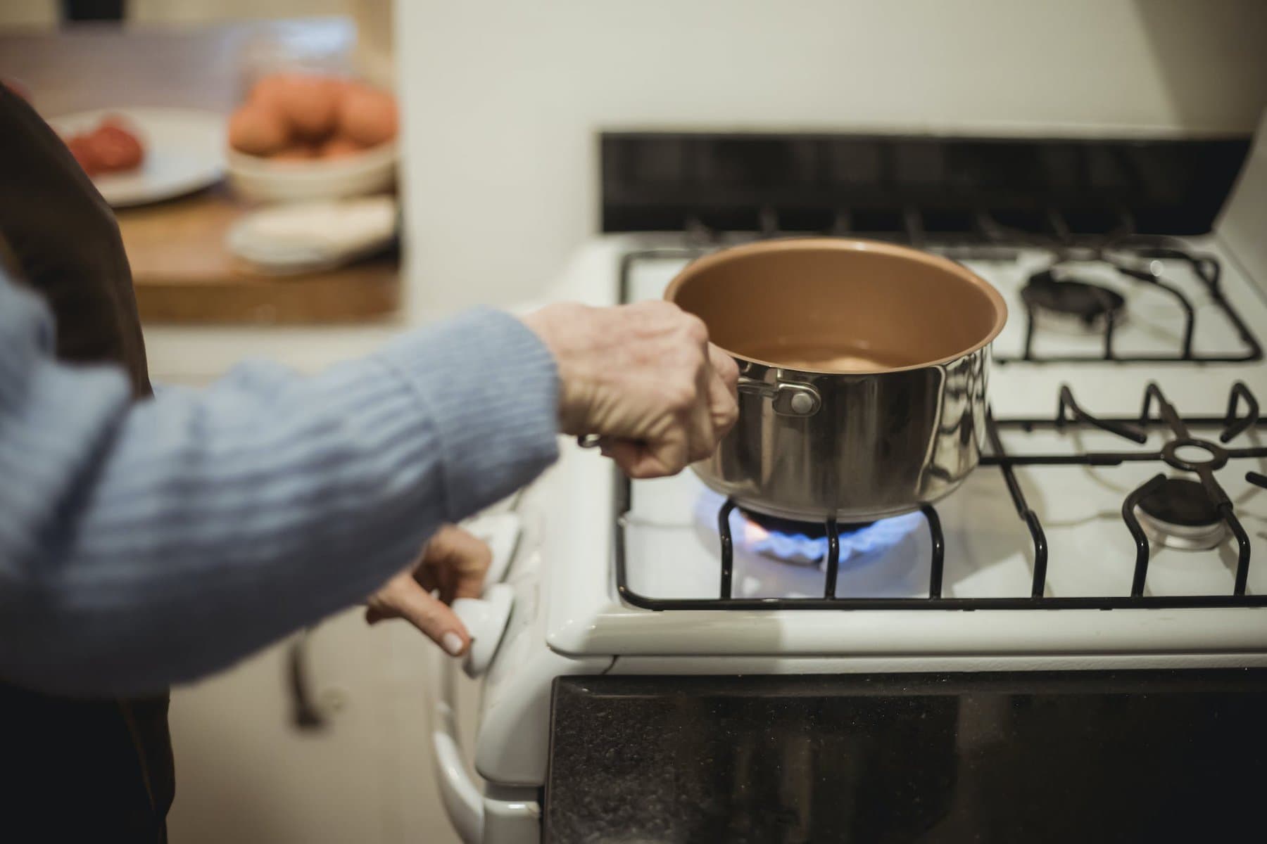 woman placing saucepan on burning stove to boil chicken